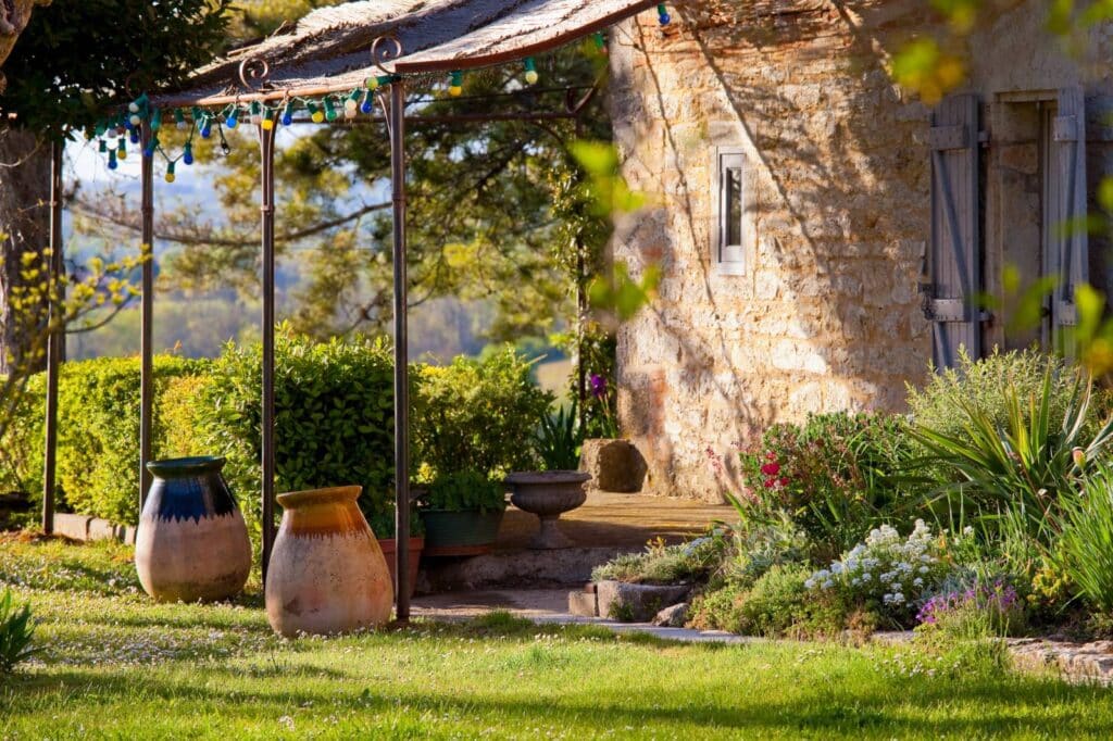 Pot en terre cuite et verdure devant une maison en pierre sous un ciel ensoleillé