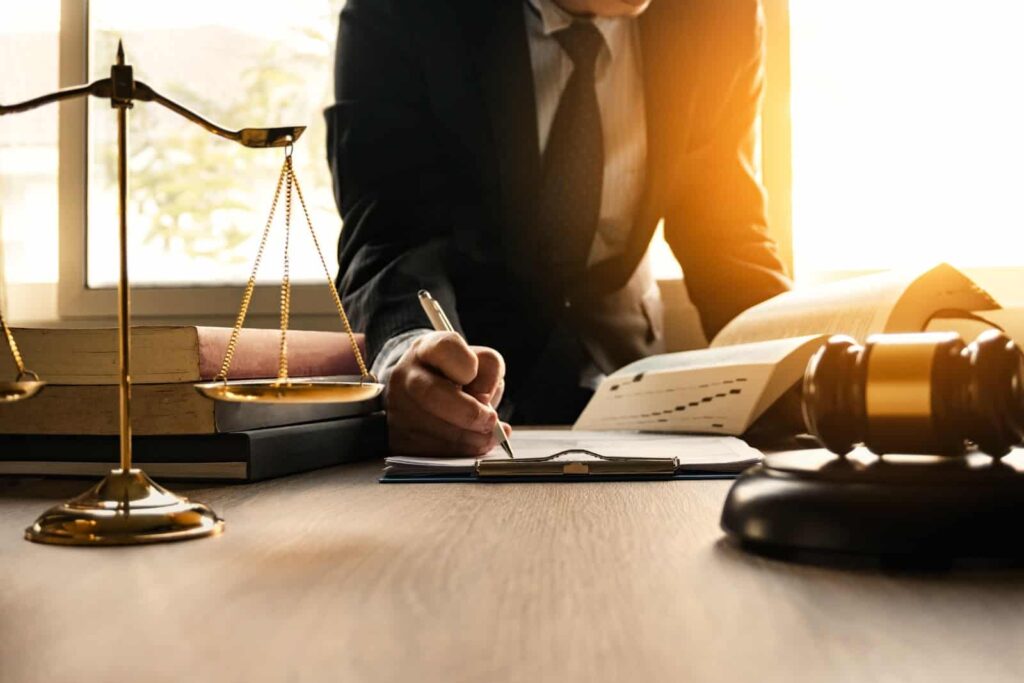 Avocat rédigeant un document avec balance de la justice, marteau et livres. Étude de droit, justice, contrats.